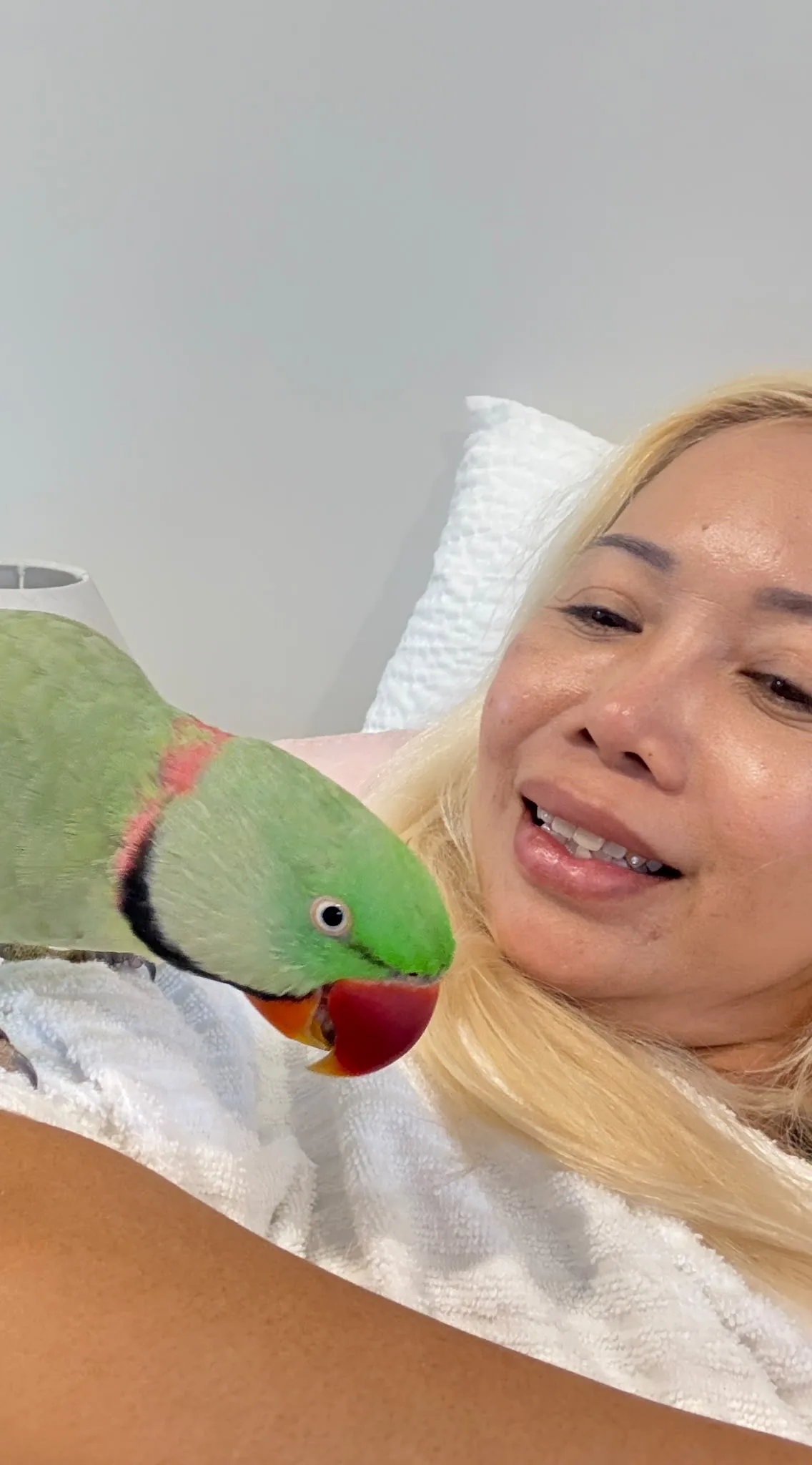 Malee smiling as a green parrot leans towards her while perched on her arm.
